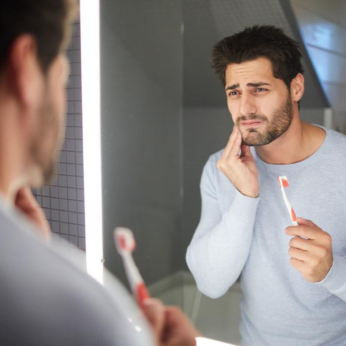 man holding toothbrush and jaw in pain