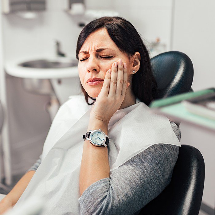 woman wearing watch wincing in pain and holding jaw