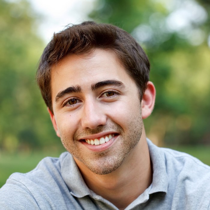 Man in grey collared shirt smiling outside