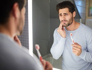 man holding toothbrush and cheek in pain