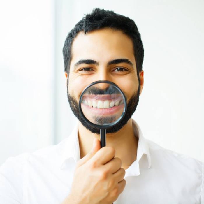  man in white dress shirt holding magnifying glass to his smile 
