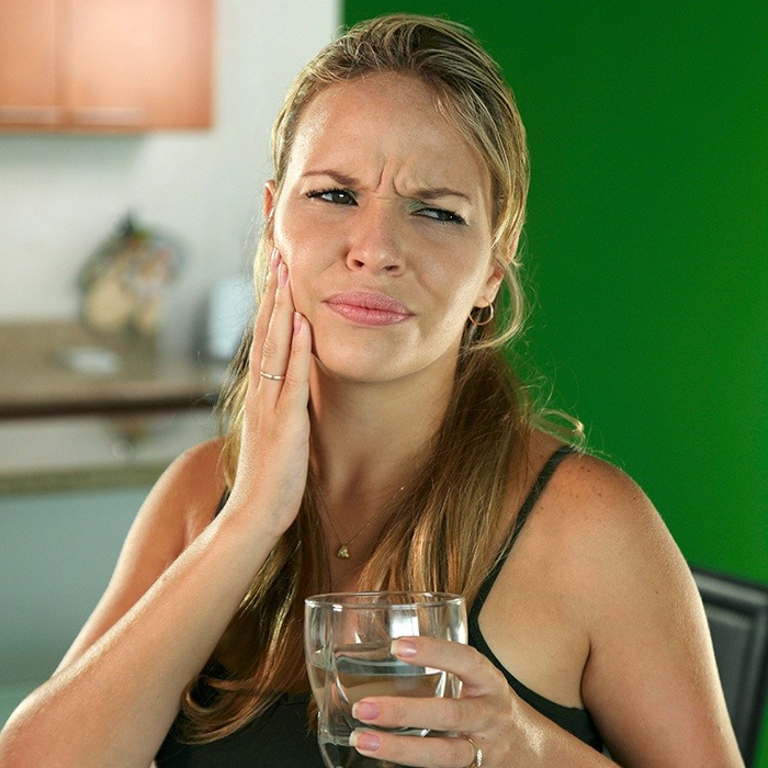 woman holding glass of water and cheek in pain