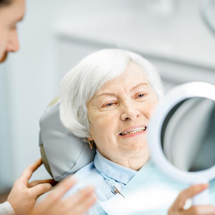 Older woman with implant smiling into hand mirror