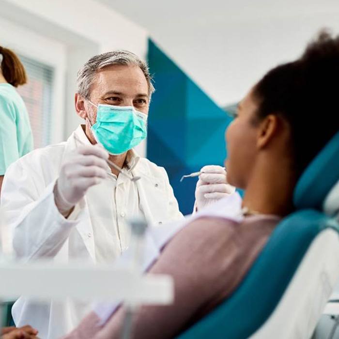 Masked dentist approaching patient with dental instruments