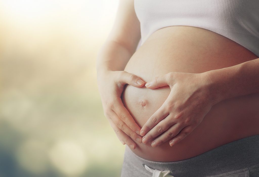 Woman making a heart shape over stomach during pregnancy